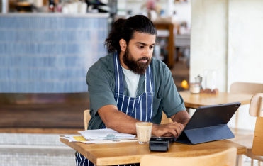 Person in apron working on laptop at cafe table